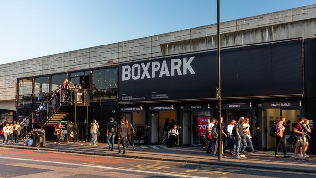 Check out small shops in old shipping containers at Boxpark Shoreditch. ©Visit London. The exterior of container village Boxpark in Shoreditch, with shoppers and people queuing for the restaurants