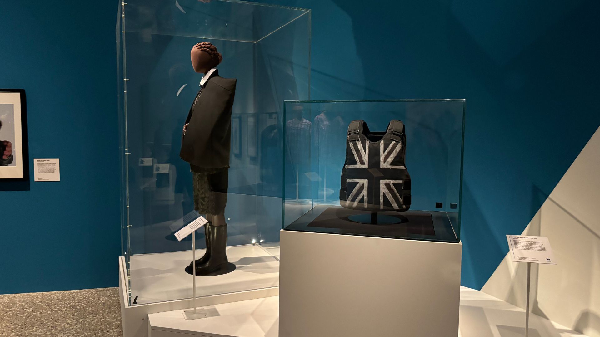 Discover Stormzy’s Banksy designed Glastonbury vest and fashion worn by Little Simz at The Music is Black: A British Story. © Visit London/Charlotte Pritchard. Stormzy’s Banksy designed Glastonbury vest in a display case with an outfit worn by Little Simz behind.