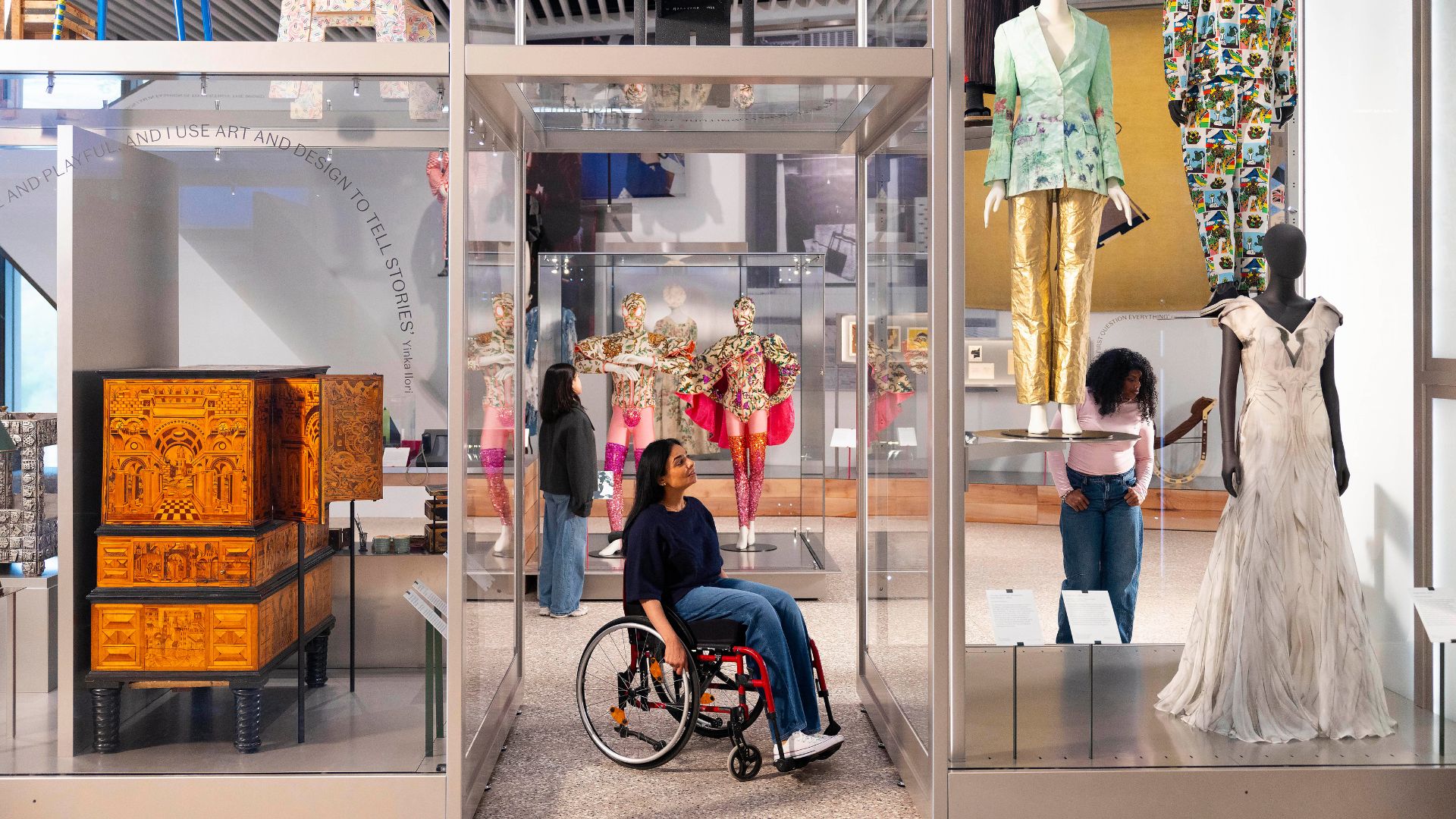 Explore the V&A East Museum designed by O’Donnell + Tuomey © David Parry for the V&A. Image courtesy of V&A East. Museum exhibits arranges in a shop front formation with costumes in glass case.