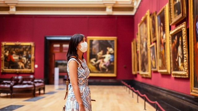 National Gallery. Credit: London & Partners/Peter Kindersley. Image courtesy of London & Partners/Peter Kindersley. A person wearing a mask admires a wall filled with paintings at the National Gallery.