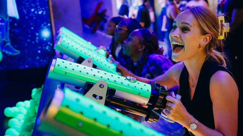 Test out your skills with fun games at Fairgame City. Image courtesy of Klaxonn. A person smiling as they aim a green toy cannon at a target.