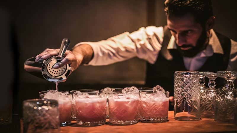Smuggle in liquor and enjoy bespoke cocktails at the Moonshine Saloon. Credit: Golden Tours. Image courtesy of Golden Tours. A bartender pouring cocktails into small tumble glasses lined up in a row