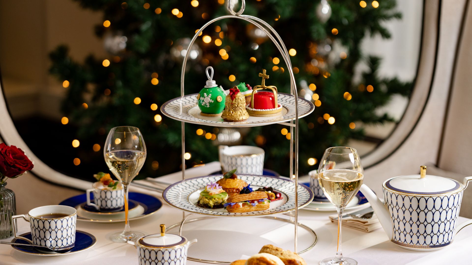 Festive afternoon tea at Intercontinental London Park Lane. Image courtesy of Roche Communications. festive afternoon tea presented on a white cloth table with fine china tea cups and a lit Christmas tree in the background