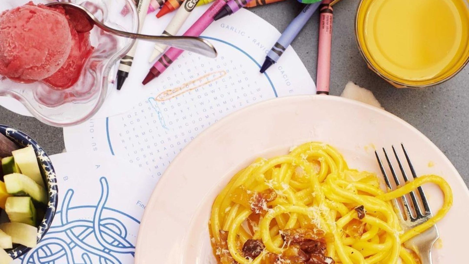 Fresh pasta dishes served at Pastaio, a lively Italian spot known for handmade pasta and family-friendly menus. Image courtesy of Pastaio. A bowl of spaghetti pasta with grated cheese on a table beside crayons, a colouring sheet, fruit pieces and a dessert dish.