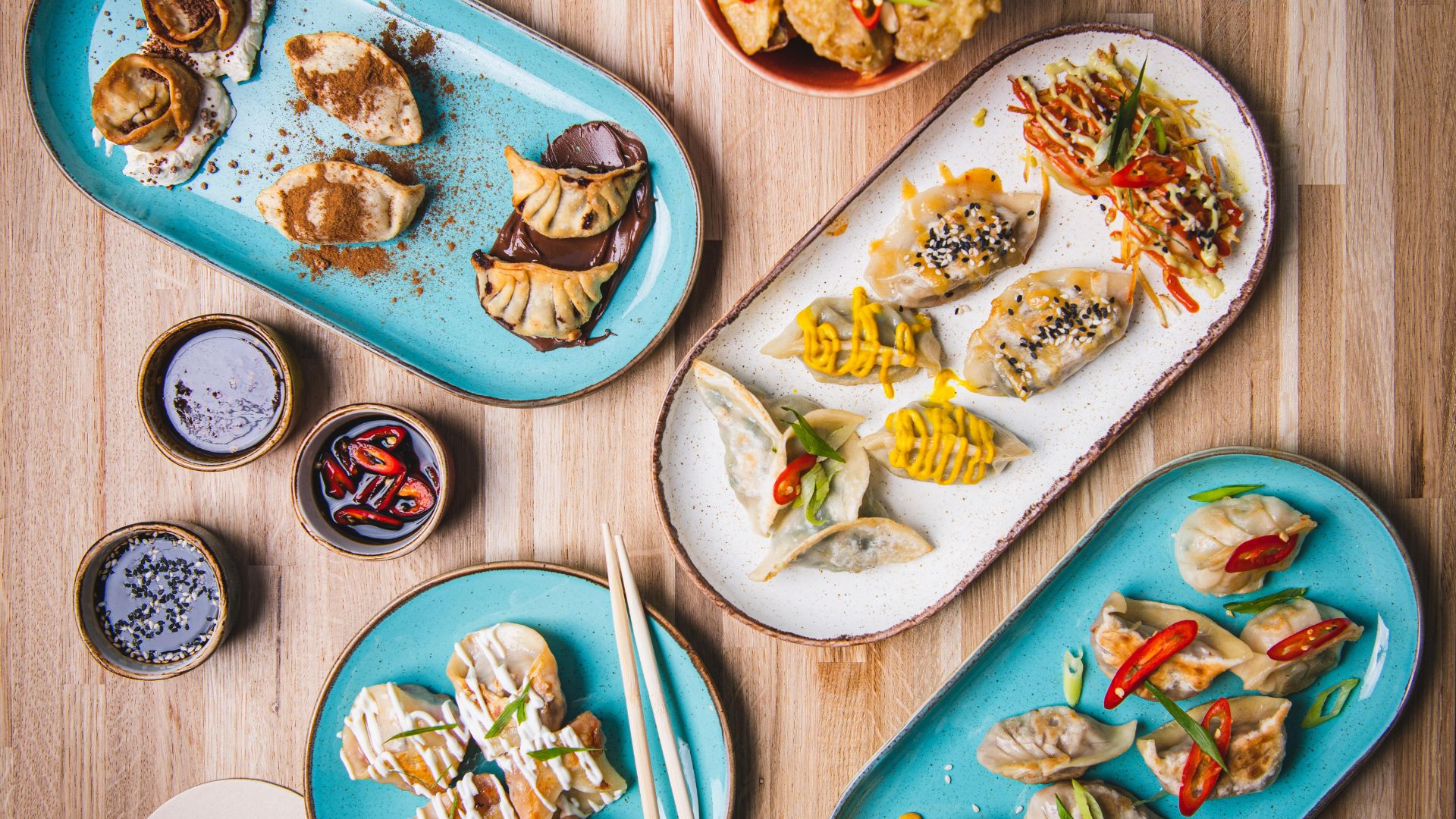 Creative dumpling dishes served at Ugly Dumpling, where sweet and savoury fillings bring a playful twist to the classic dumpling. Image courtesy of Ugly Dumpling. Several plates of dumplings with different toppings and sauces arranged on a wooden table alongside dipping sauces and chopsticks.