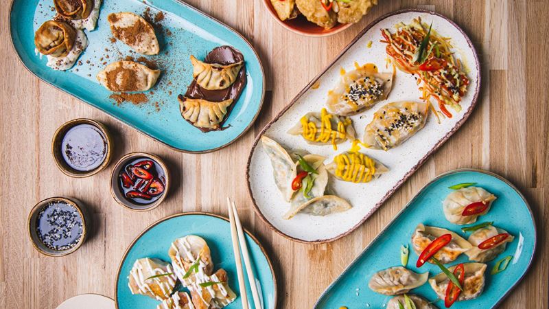 Creative dumpling dishes served at Ugly Dumpling, where sweet and savoury fillings bring a playful twist to the classic dumpling. Image courtesy of Ugly Dumpling. Several plates of dumplings with different toppings and sauces arranged on a wooden table alongside dipping sauces and chopsticks.