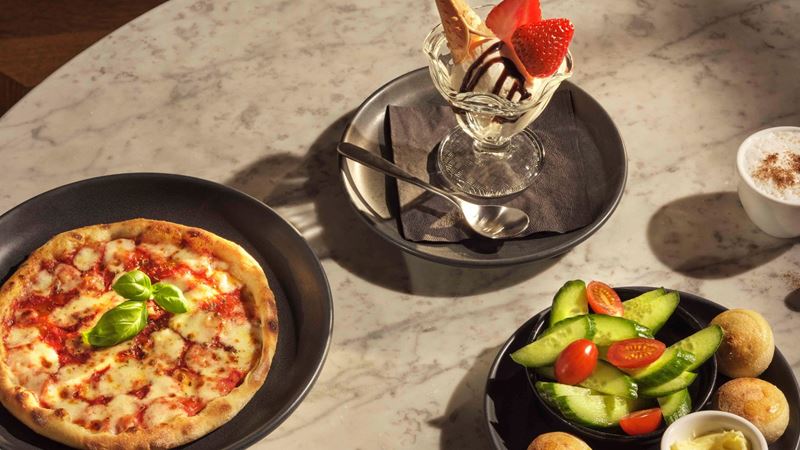 From mini pizzas to crunchy veggies and an indulgent sundae, the Piccolo children’s menu at PizzaExpress turns family dining into a fun and flavour-packed experience for younger guests. Image courtesy of Pizza Express. A children’s meal at PizzaExpress with a small pizza, cucumber and tomato salad, dough balls and an ice cream sundae on a table.