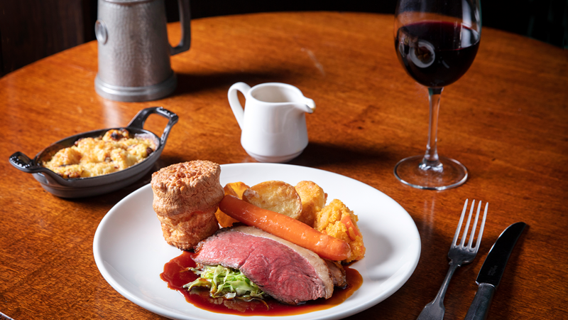 Choose from several tempting roasts, including the roast beef with seasonal vegetables and gravy. Credit: The Audley Public House, Mayfair. Image courtesy of The Audley Public House, Mayfair. A plate of roast beef, vegetables, Yorkshire pudding and gravy, a glass of wine and cutlery.