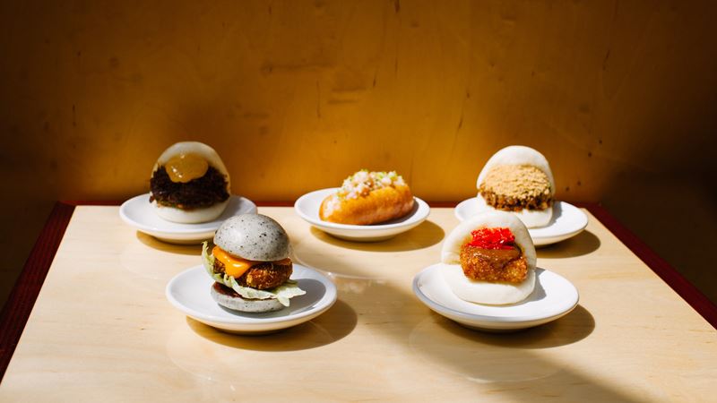 Bao buns at Taiwanese restaurant Bao Borough. Image courtesy of Bao. Four small plates, each with fluffy bao buns with different fillings, on a light-coloured wooden table top.