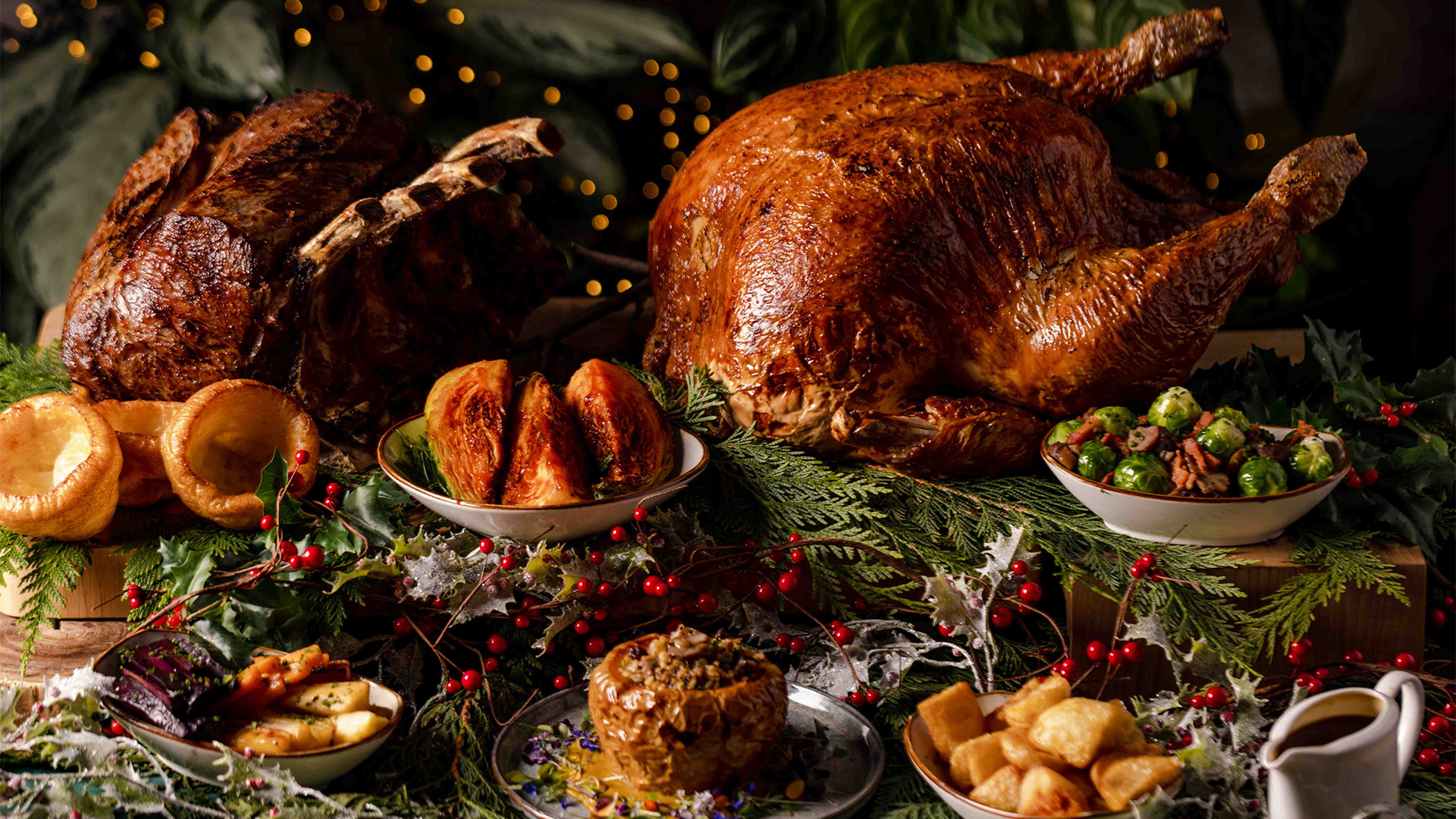 Christmas Day dinner by Pan Pacific London. Credit: Pan Pacific London. Image courtesy of Pan Pacific London. A golden roast turkey sits on a table alongside bowls of crispy roast potatoes, cabbage, brussel sprouts, parsnips and yorkshire puddings.