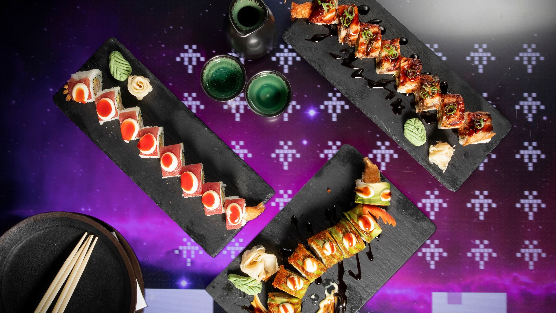 Colourful sushi rolls and Japanese small plates served at inamo, where interactive tables let diners play games and explore the menu while they eat. Image courtesy of Inamo. Assorted sushi rolls arranged on black serving plates with dipping sauces and drinks on a table with a digital interactive surface.