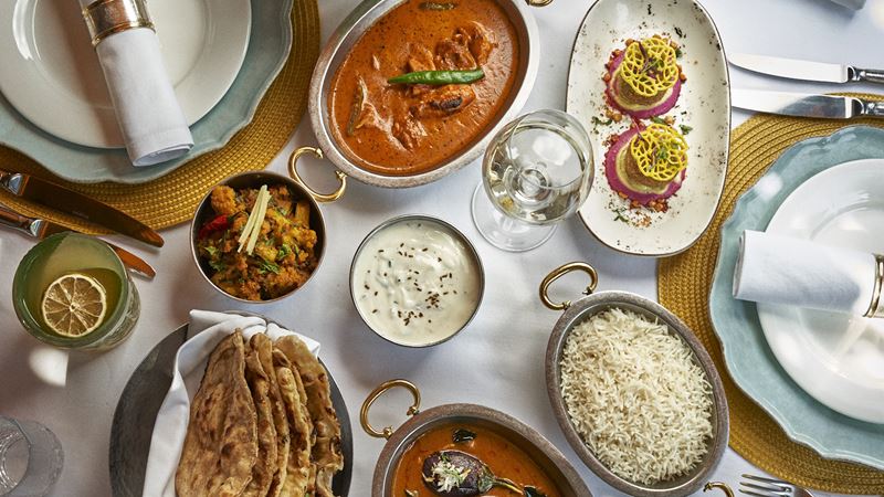 Discover a Michelin-star menu that showcases the diverse flavours of the Indian subcontinent. Credit: Jamavar. Image courtesy of Jamavar. Indian dishes laid out on table with white tablecloth, including curry, rice, dips and naan bread.