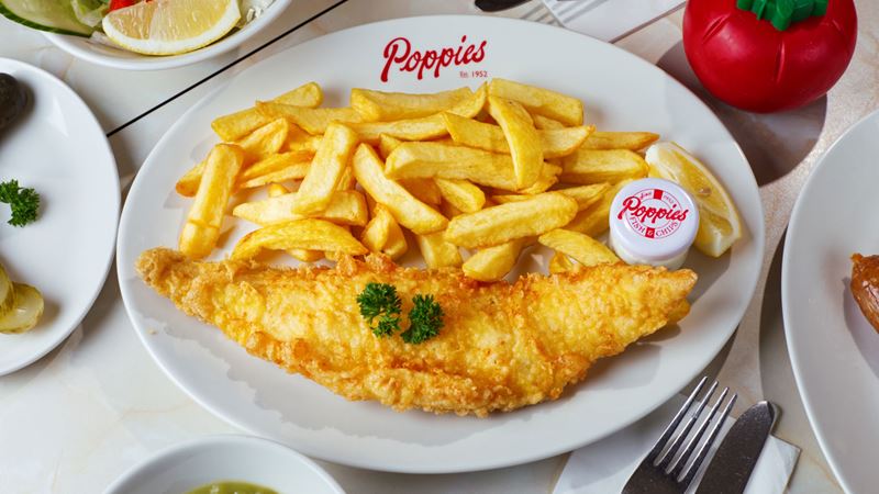 Tuck into a proper plate of fish and chips at Poppies. Credit: Stacie Ma Photography. Image courtesy of Poppies. A birds eye photo of a plate of battered fish and chips garnished with parsley on a plate with the Poppies logo