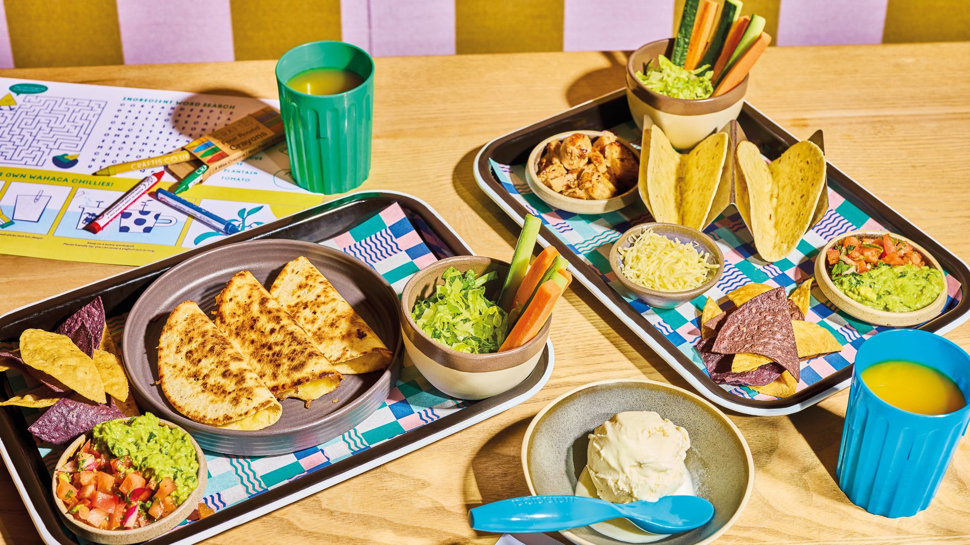 Tacos, quesadillas and colourful sides from the kids’ menu at Wahaca, served with activity sheets to keep younger diners entertained. Image courtesy of Wahaca. A children’s Mexican meal including quesadillas, tacos, guacamole, chips and vegetables on trays with crayons and activity sheets.