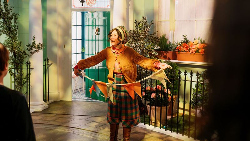 Meet characters inspired by the Paddington books and films at The Paddington Bear Experience. Image courtesy of Golden Tours. A woman interpreting Mrs Brown at the Paddington Bear Experience holds buntings in front of visitors.