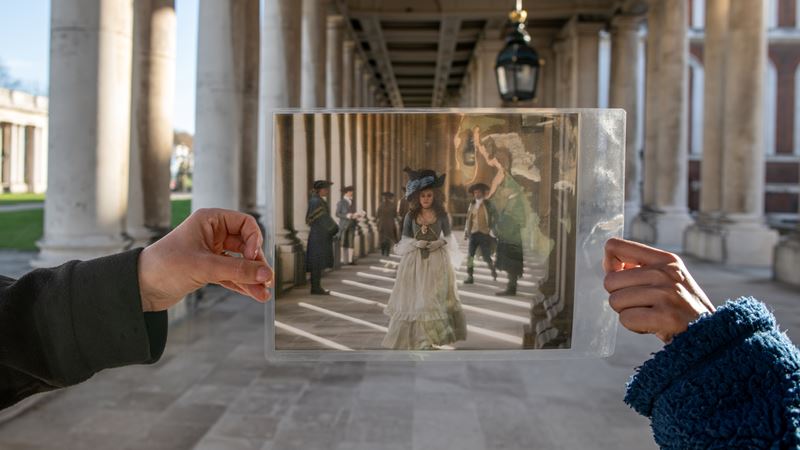 Tour the famous film locations scattered around the Old Royal Naval College grounds. Credit: London & Partners/Michael Barrow. Image courtesy of London & Partners. A photo of someone holding up a photo of a still from Bridgerton in front of the site it was filmed at a walkway on the Old Royal Naval College grounds
