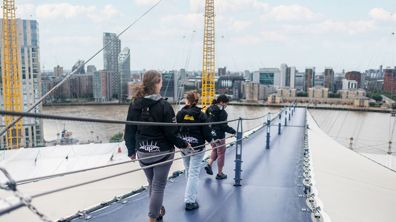 Get ready for an exhilarating adventure and views to remember during Up at The O2. Credit: London & Partners/Michael Barrow. Image courtesy of London & Partners. A photo of three women scaling the roof of The O2 during Up at The O2 with a backdrop of London in the background