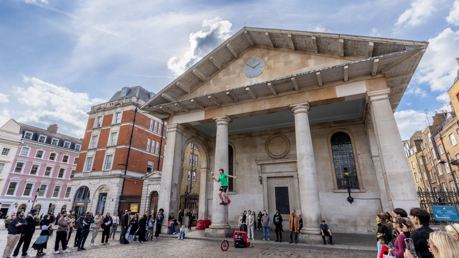 Join the crowds that flock to watch Covent Garden's street performers. Credit: London & Partners/Peter Cohen. Image courtesy of visitlondon.com. A photo of a man on a giant unicycle juggling in front of crowds of people in the main square of Covent Garden