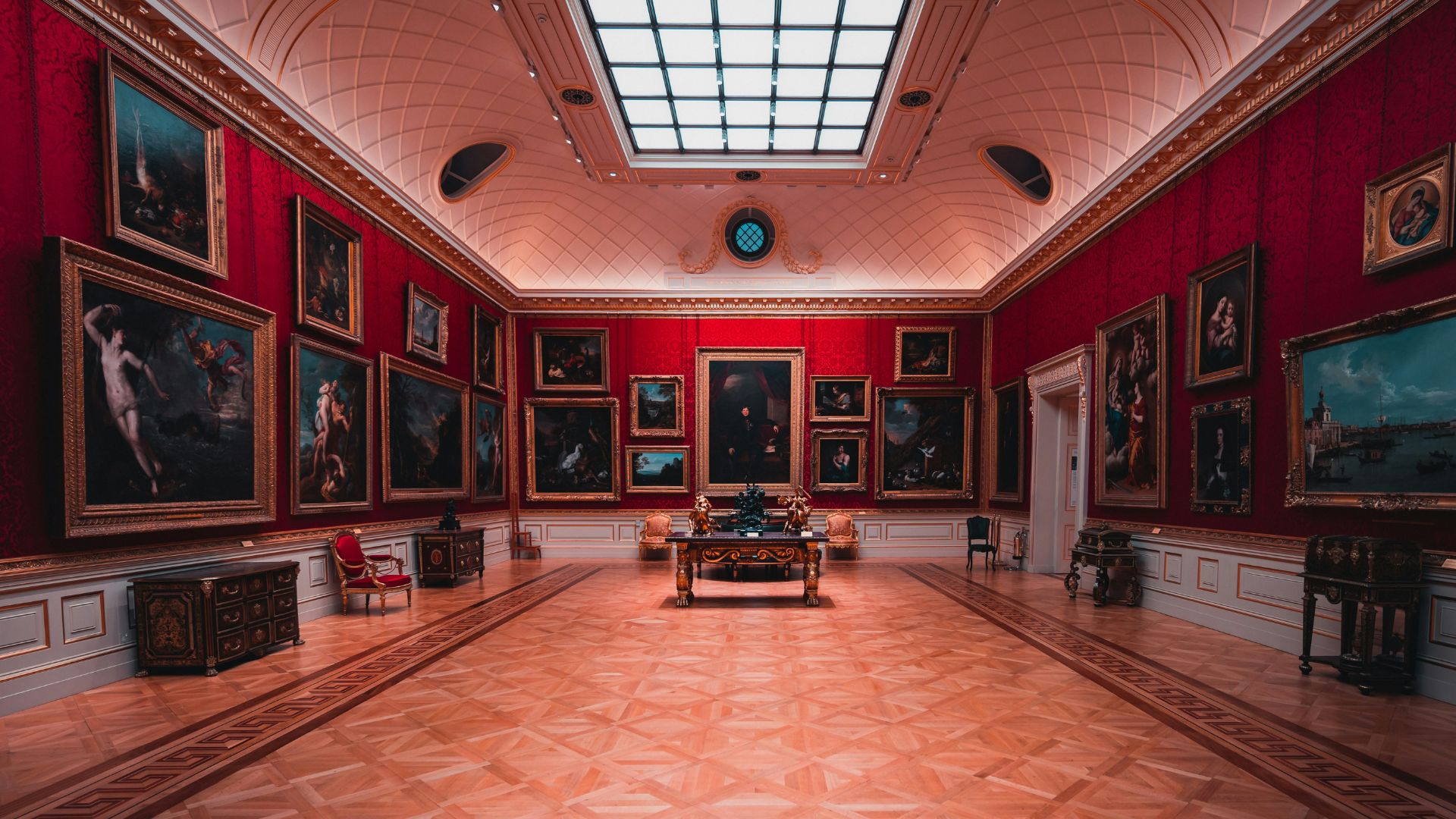 Explore European art at The Wallace Collection. Image courtesy of Unsplash. View of The Wallace Collection gallery with red walls and paintings displayed on each.