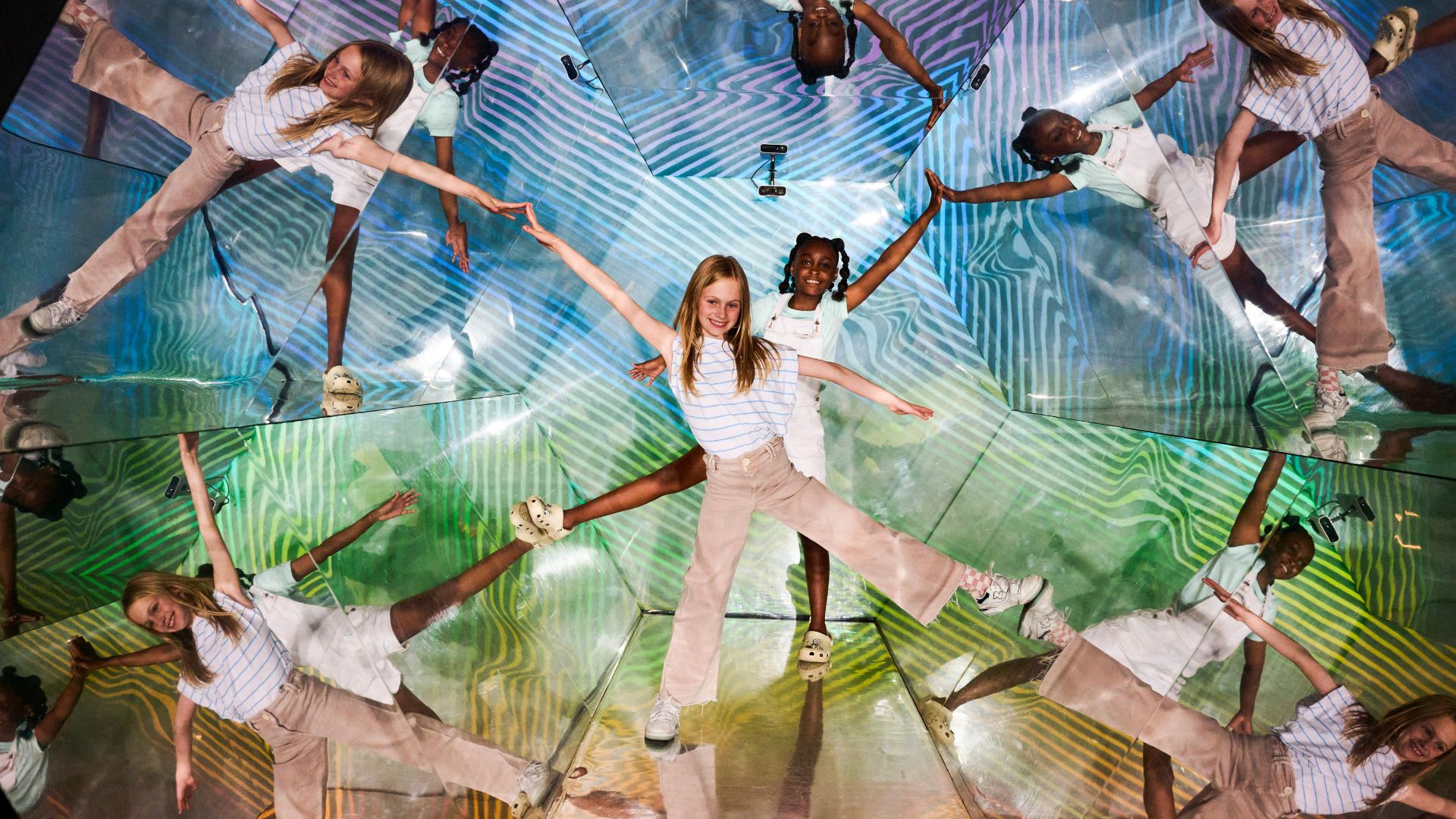 Snap fun illusions at Twist Museum. Image courtesy of Twist Museum. Two children standing in illusion room with multiple reflections of themselves surrounding them.