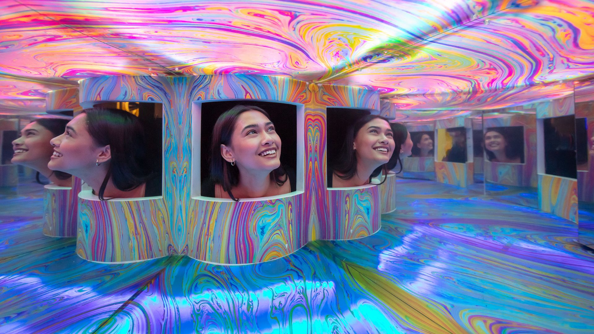 Discover transformative colour experiences at Twist Museum. Image courtesy of Twist Museum. Person looking into colourful mirrored illusion room at Twist Museum.