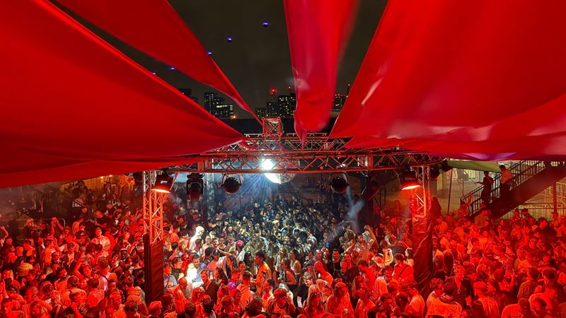 Enjoy open-air parties from day to night at The Cause. Credit: Lucie Fryer. Image courtesy of Lucie Fryer. A photo of an outdoor stage at The Cause in London with a giant disco ball and red tapestry hanging over a large crowd of people