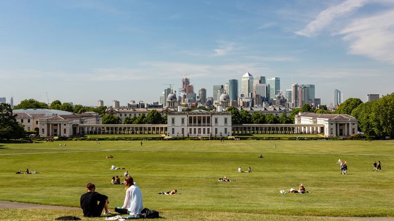 Take in one of the best London views from Greenwich Park. Credit: London & Partners/Jon Reid. Image courtesy of visitlondon.com. Groups of people sit on the hill of Greenwich Park overlooking the Old Royal Naval College and the London skyline.