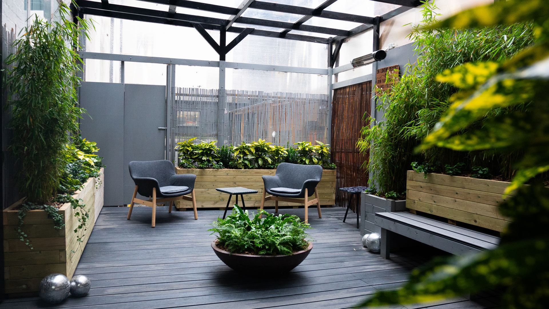 Enjoy modern and comfortable rooms at The Wesley in Camden, and relax in the outdoor courtyard. Credit: Robin Prime. Image courtesy of The Wesley. Grey seats and benches in a covered courtyard lined with green plants in wooden troughs and a bowl of ferns in the middle of the space.
