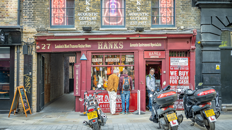Explore renowned Hank's Guitar Shop in Soho, offering vintage, electric, acoustic, bass and more. Credit: Shutterstock. Image courtesy of Shutterstock. Red exterior storefront of Hank's Guitar Shop with three motorbikes parked up in front
