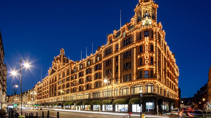 Experience Harrods, a world‑famous luxury department store and one of London’s most famous shopping destinations © visitlondon.com/Jon Reid. Image courtesy of visitlondon.com/Jon Reid. Harrods department store lit up at night against a dark blue sky and illuminated street lights in London.