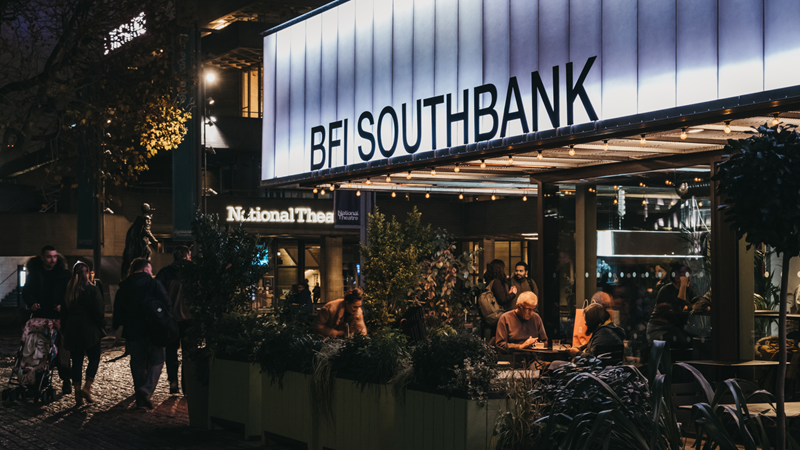 Look out for exciting events at BFI Southbank alongside an exciting range of films every day of the week. Credit: Shutterstock. Image courtesy of Shutterstock. An image of the front of BFI Southbank at night with groups of people sat outside at tables and walking in front of the building with lights illuminating the venue