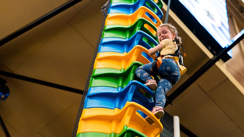 Enjoy a climbing experience for all ages at Clip 'n Climb. Credit: NB Photography. Image courtesy of Clip 'n Climb. A young girl looking down as she climbs a multicoloured climbing frame at Clip 'n Climb.