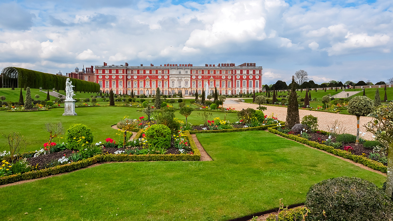 Walk through the magnificent gardens of Hampton Court Palace. Image courtesy of Shutterstock. A long walkway leads to the brick Tudor Palace of Hampton Court, borered by flower beds and French-inspired landscaping.