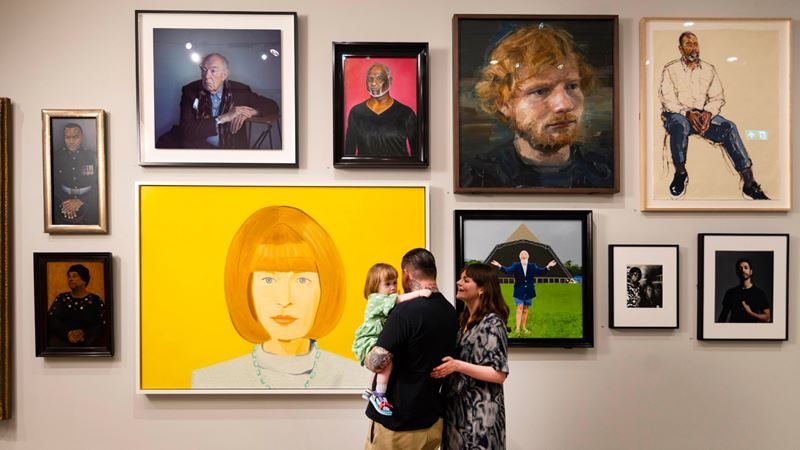 The National Lottery Heritage Fund Gallery at the National Portrait Gallery, London. Photography © Dave Parry. Image courtesy of National Portrait Gallery. Several portraits of famous people on gallery wall with family looking at them.