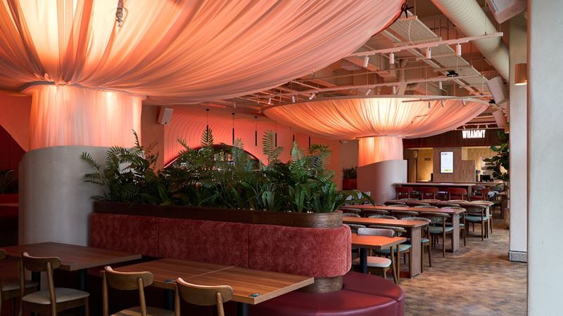 Check out Olympia's new Arbour Bar and Food Hall. Image courtesy of Olympia. Dining tables and chais with plants and hanging lights inside an empty food hall.