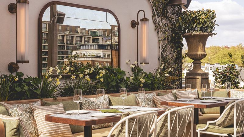 Unwind at Lillie's, an elegant rooftop terrace inspired by the charm of an English garden. Image courtesy of Olympia. An elegant rooftop terrace inspired by the charm of an English garden with small tables and chairs, plants and hanging lights.