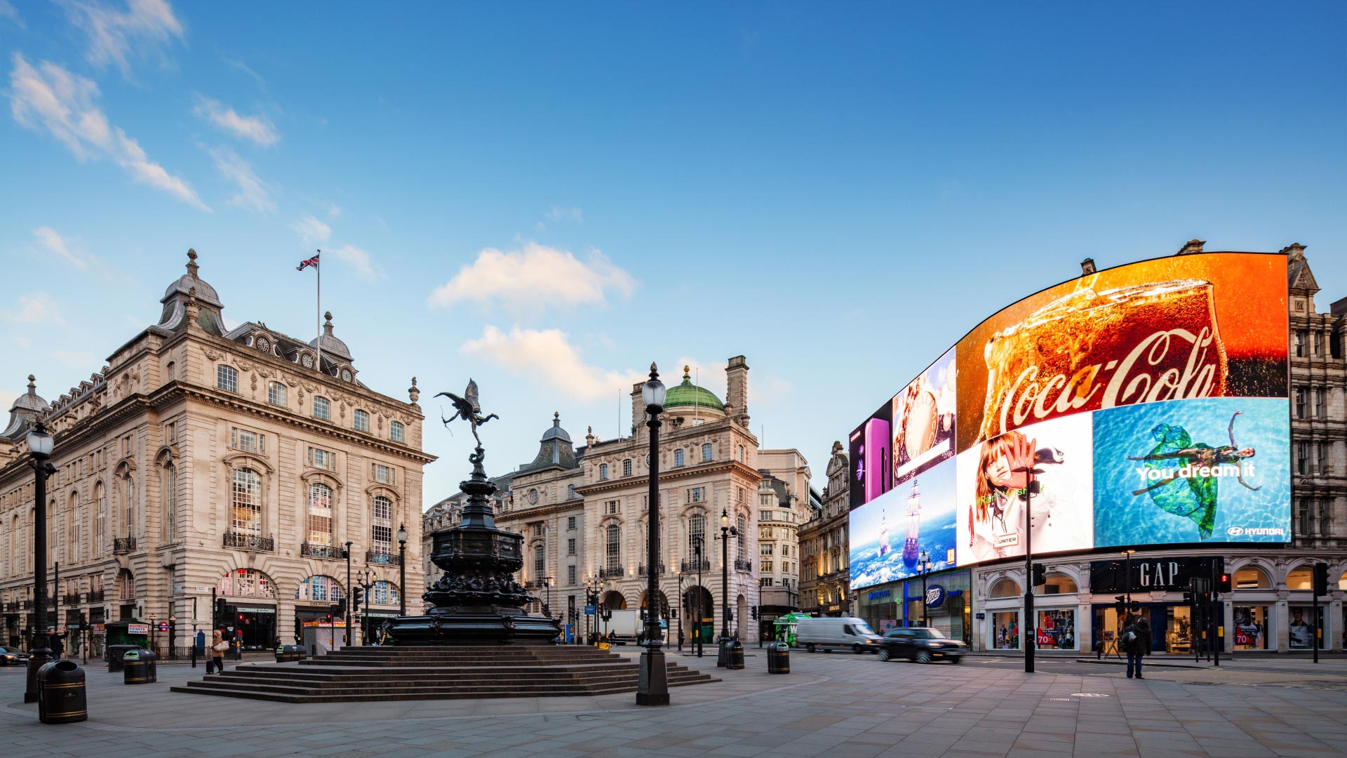 Explore the historic shops of St James's and the vibrant Piccadilly area. Image courtesy of visitlondon.com/Jon Reid. A wide-angle view of Piccadilly Circus on a bright day, with the statue of Eros in the foreground and the famous wall of LED lights illuminated on the right