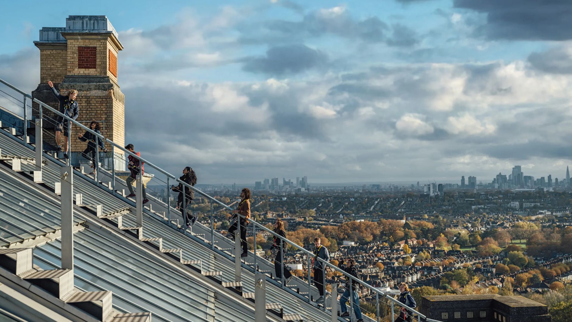 Climb the iconic Ally Pally rooftop to the Angel of Plenty statue for breathtaking 360-degree views across the capital. Image courtesy of Golden Tours. People climbing the rooftop steps of Alexandra Palace with panoramic views of London in the background.