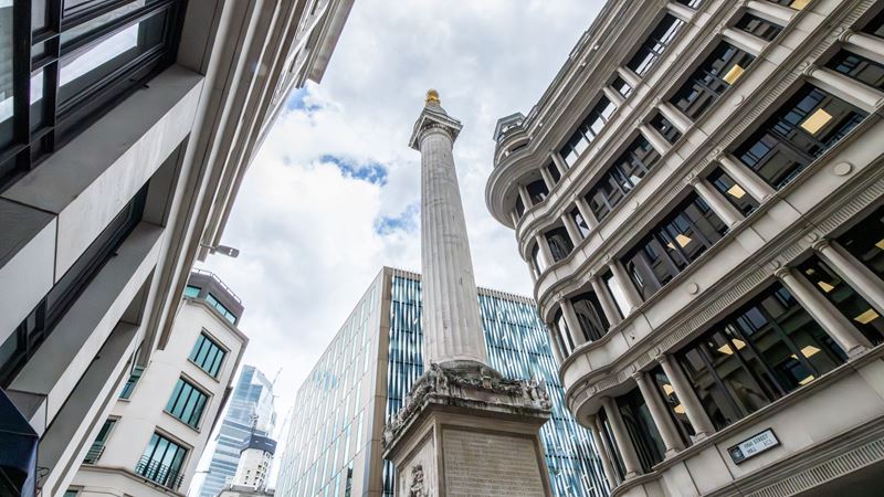 Climb the 311 steps of The Monument © London & Partners/Michael Barrow. A view looking up at The Monument, with modern buildings either side.