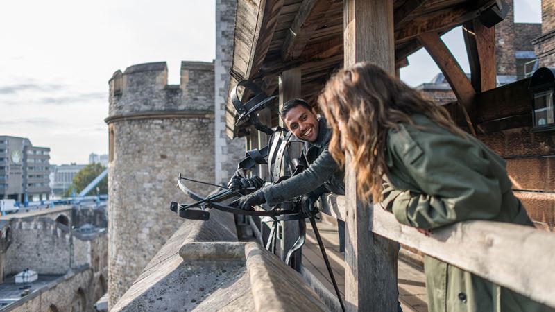 Imagine what it was like to live inside the Tower of London as you walk along the fortifications. Credit: Michael Barrow. Image courtesy of London & Partners. Two people stand on the stone battlements next to a crossbow on the tower of london.