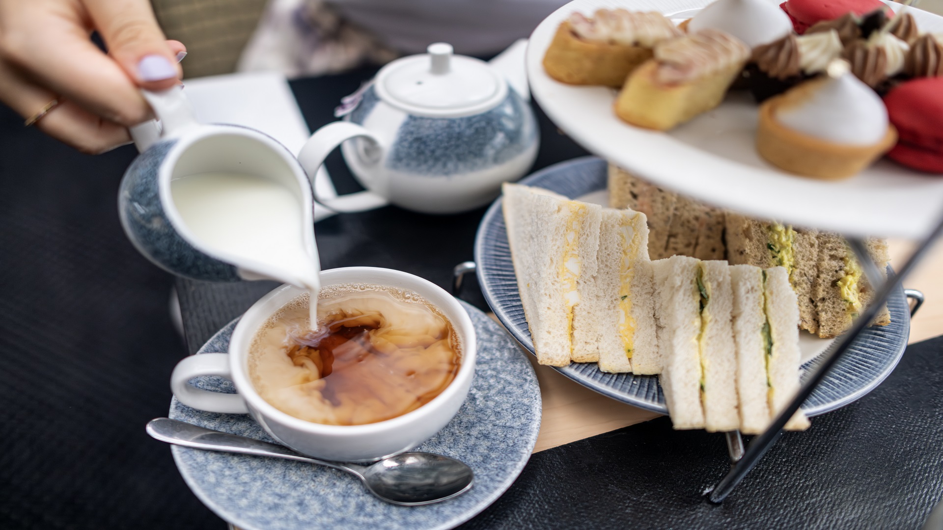Escape the crowds and enjoy an afternoon tea as you glide along the Thames onboard a City Cruises boat. © London & Partners/Michael Barrow afternoon tea stand with sandwiches and sweet treats, and a person pouring milk into a cup of tea