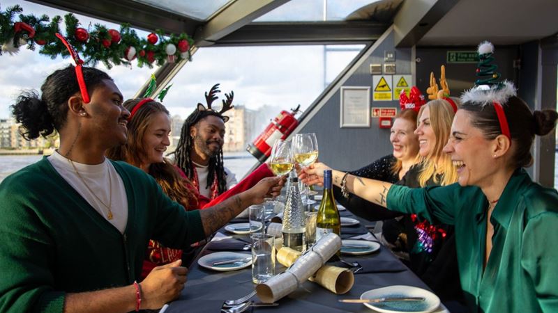 Get in the festive spirit onboard the Christmas Day traditional lunch cruise on the river Thames. Credit: Golden Tours. Image courtesy of Golden Tours. A crowd of people wearing festive costumes enjoying a Christmas Day lunch aboard a cruise.