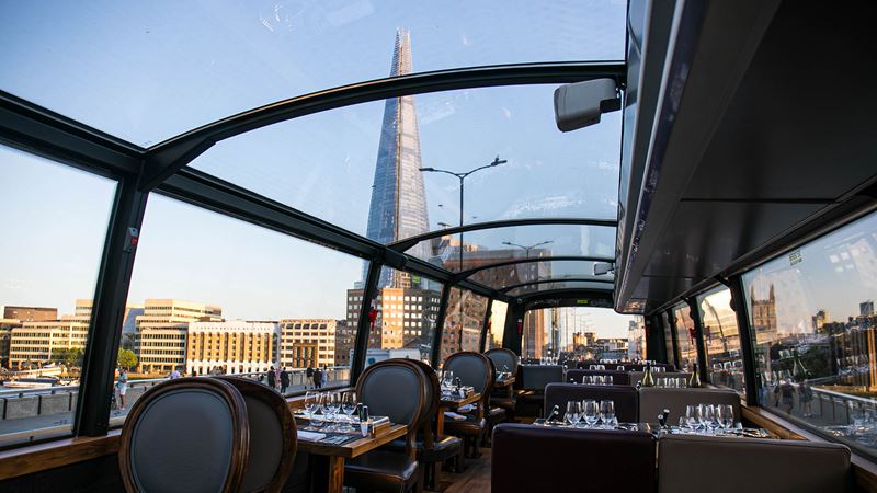 Pair sightseeing and delicious food on a Bustronome tour. Credit: Bustronome. Image courtesy of Golden Tours. The Shard and the London skyline seen through the glass roof of a tour bus on a clear sunny day.