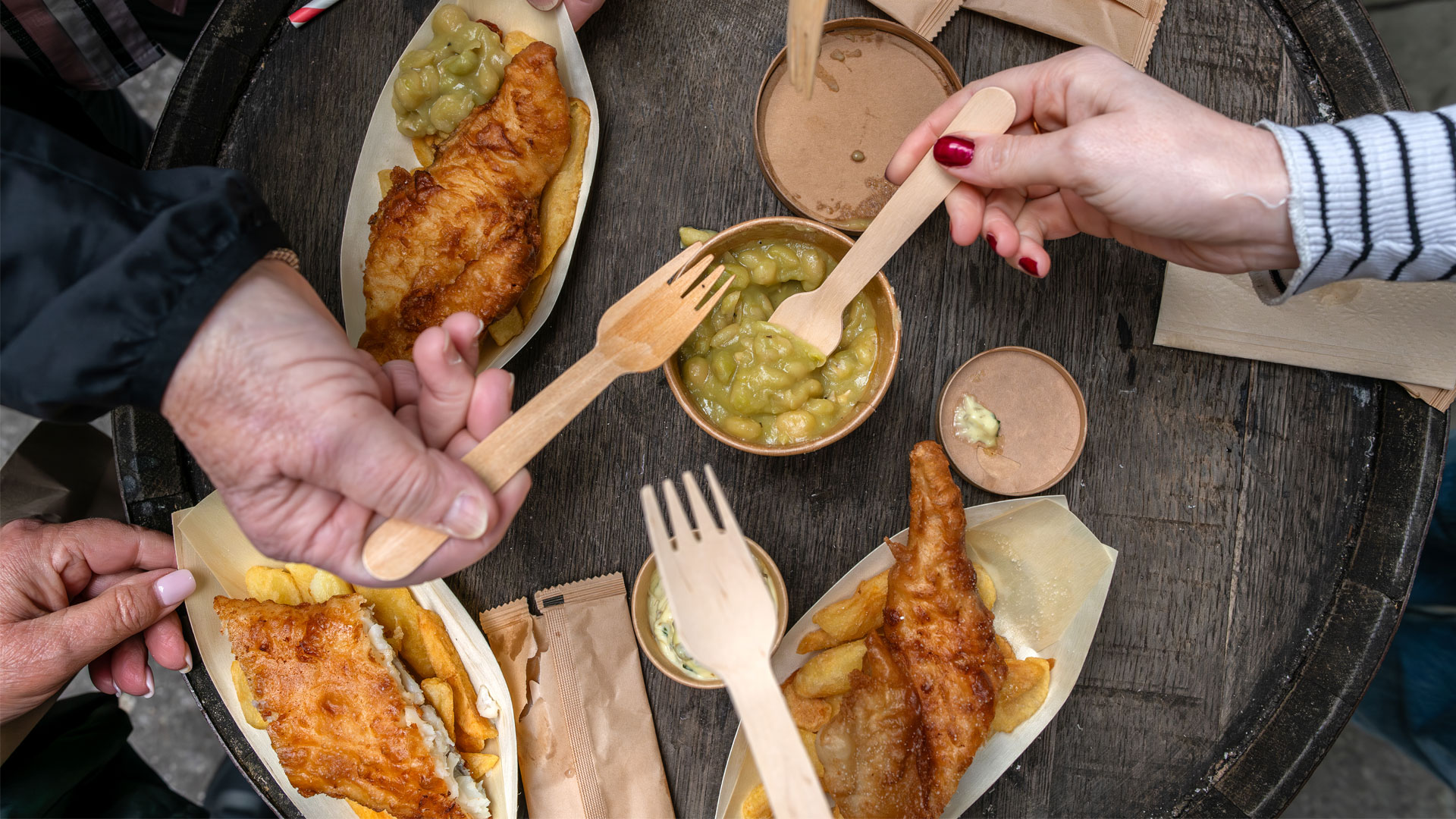 Savour a selection of classic British foods and drinks. Image courtesy of Visit London. People holding forks eating fish and chips at Borough Market.