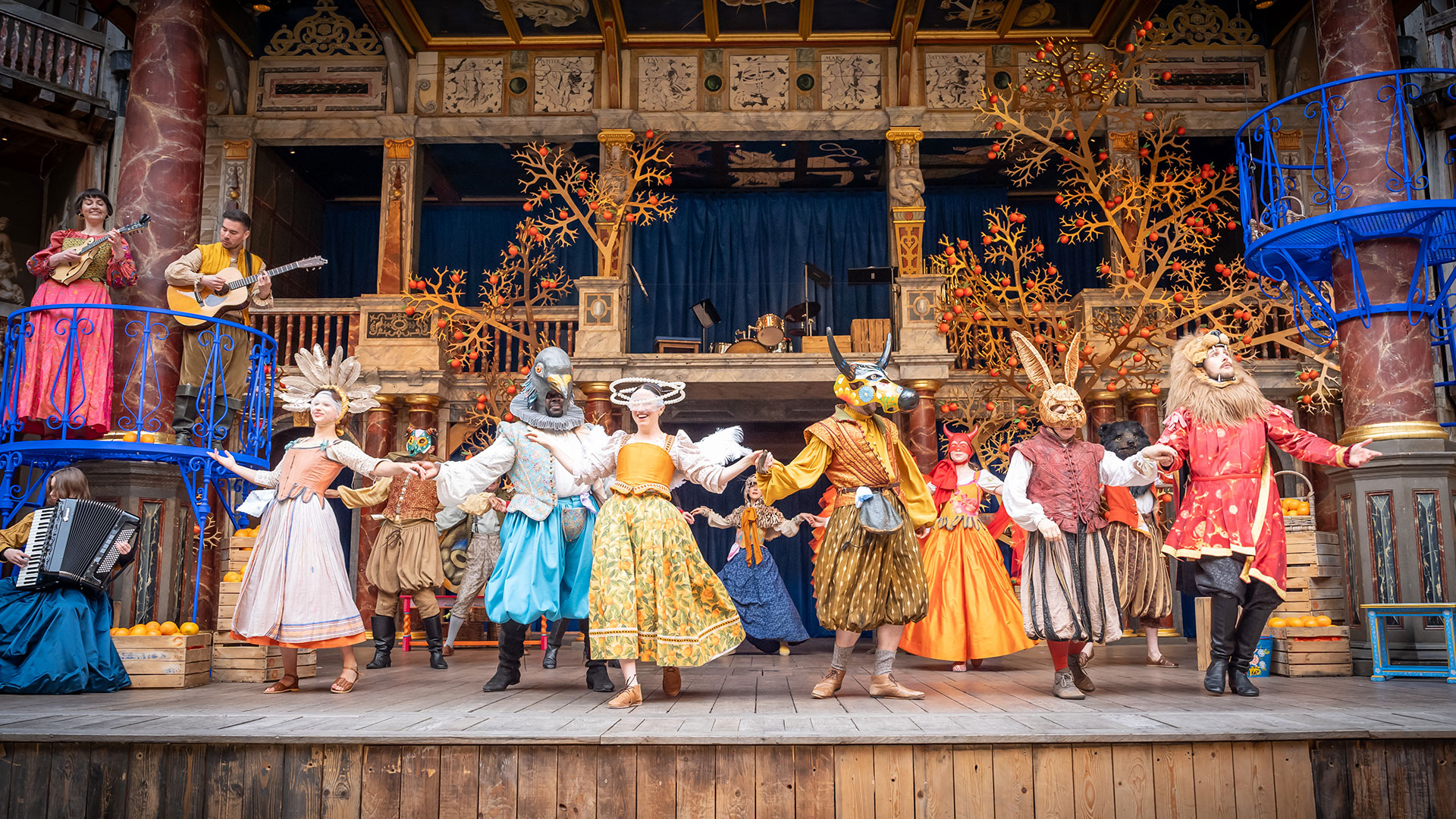 A live production of Shakespeare's comedy Much Ado About Nothing at the Shakespeare Globe Theatre in 2024. Image courtesy of the Shakespeare Globe Theatre. Actors wearing bright, colourful costumes and animal heads are dancing on the stage of the Shakespeare Globe Theatre.