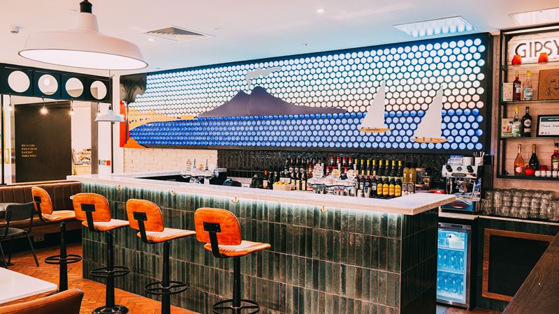 Grab a slice and enjoy the giant mural of the Bay of Naples, made from 2,000 recycled glass water bottles. Credit: Pizza Pilgrims. Image courtesy of Pizza Pilgrims. The bar at Pizza Pilgrims features a giant mural of the Bay of Naples, made using 2,000 recycled glass water bottles.