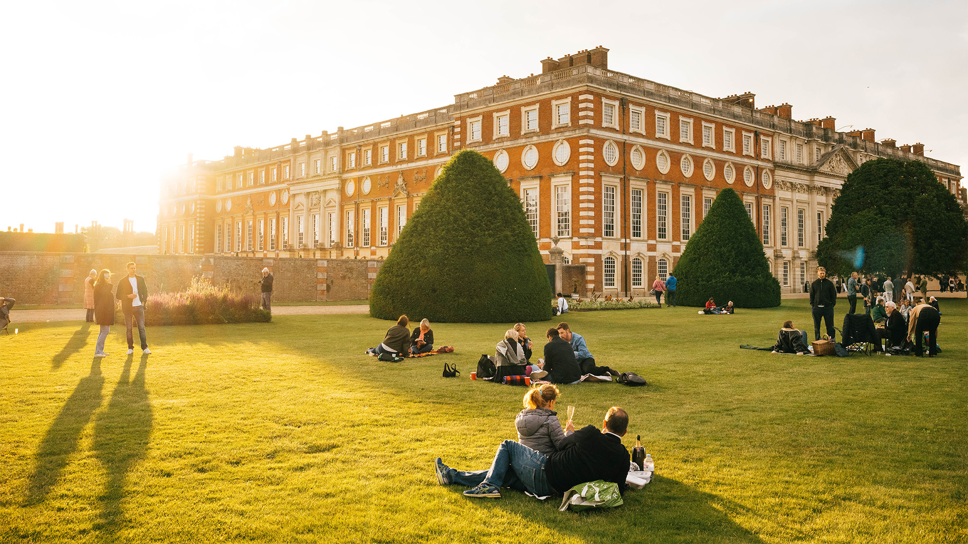 Hampton Court Palace at sunset. Image courtesy of Hampton Court Palace. Crowds picnic in the grounds of Hampton Court Palace at sunset