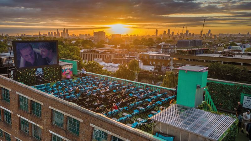 Make London's sunset the backdrop to your next movie date at Rooftop Cinema Club next in Peckham's Bussey Building. Credit: Rooftop Cinema Club. Image courtesy of Rooftop Cinema Club. A photo from above Rooftop Film Club in Peckham with the screen playing a movie to seats of people on the rooftop as the sun sets behind London's buildings in the distance