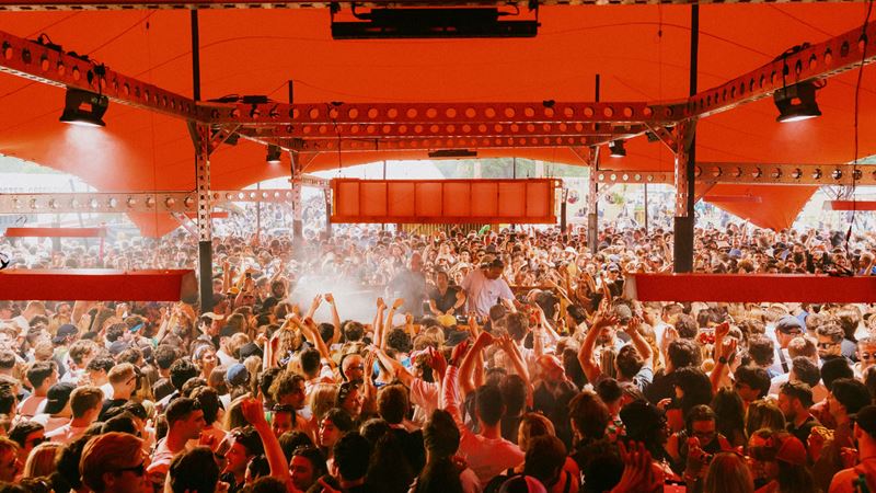 Get on your dancing gear and head to Peckham Rye in south London for Gala Festival. Credit: Jake Davis. Image courtesy of Khroma Collective. A photo of a stage at Gala festival with crowds of people stood underneath a large red rent around a stage of DJs, overhead lighting and a smoke machine