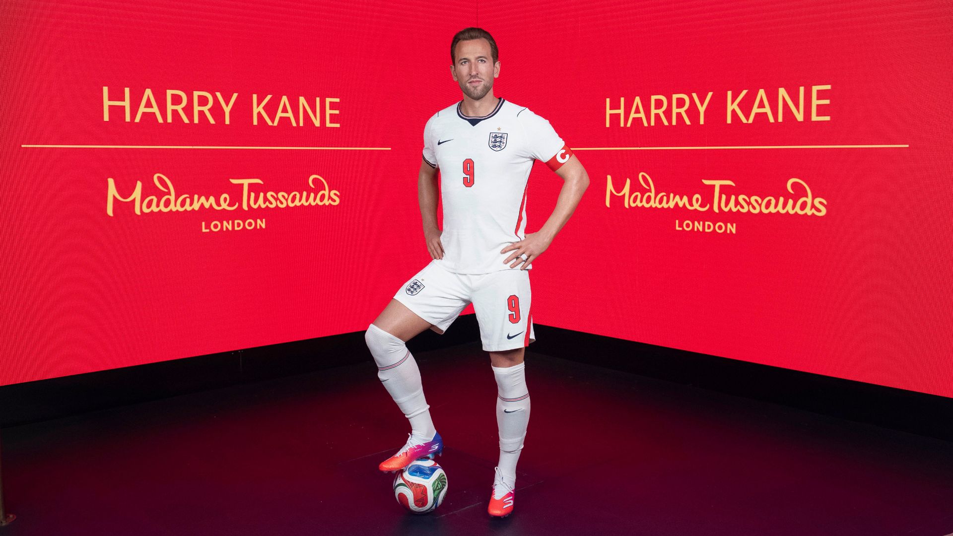 Head to Madame Tussauds to see Harry Kane's wax figure. Image courtesy of Merlin Entertainments. Wax figure of Harry Kane in full football kit with red Madame Tussauds screen behind.